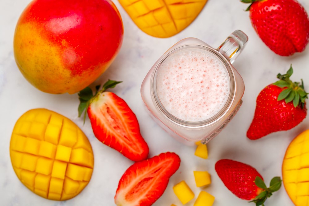 Mangos and strawberries on a marble flat lay with a creamy smoothie in a mason jar glass