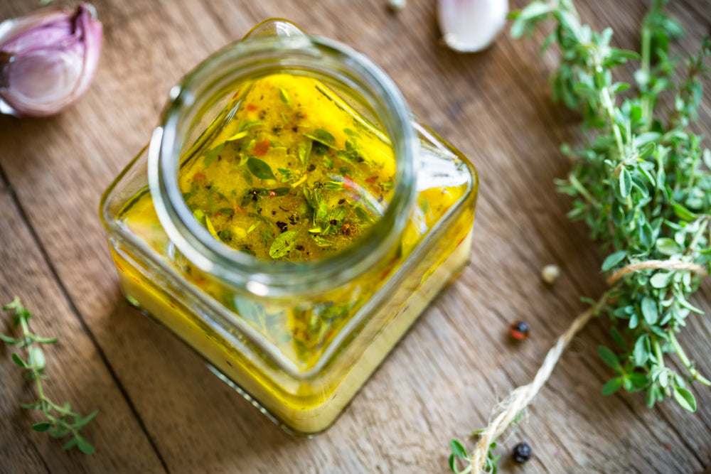 top view of a jar of pineapple chia vinaigrette dressing with herbs, onion, and peppercorn on the side on top of a wooden table