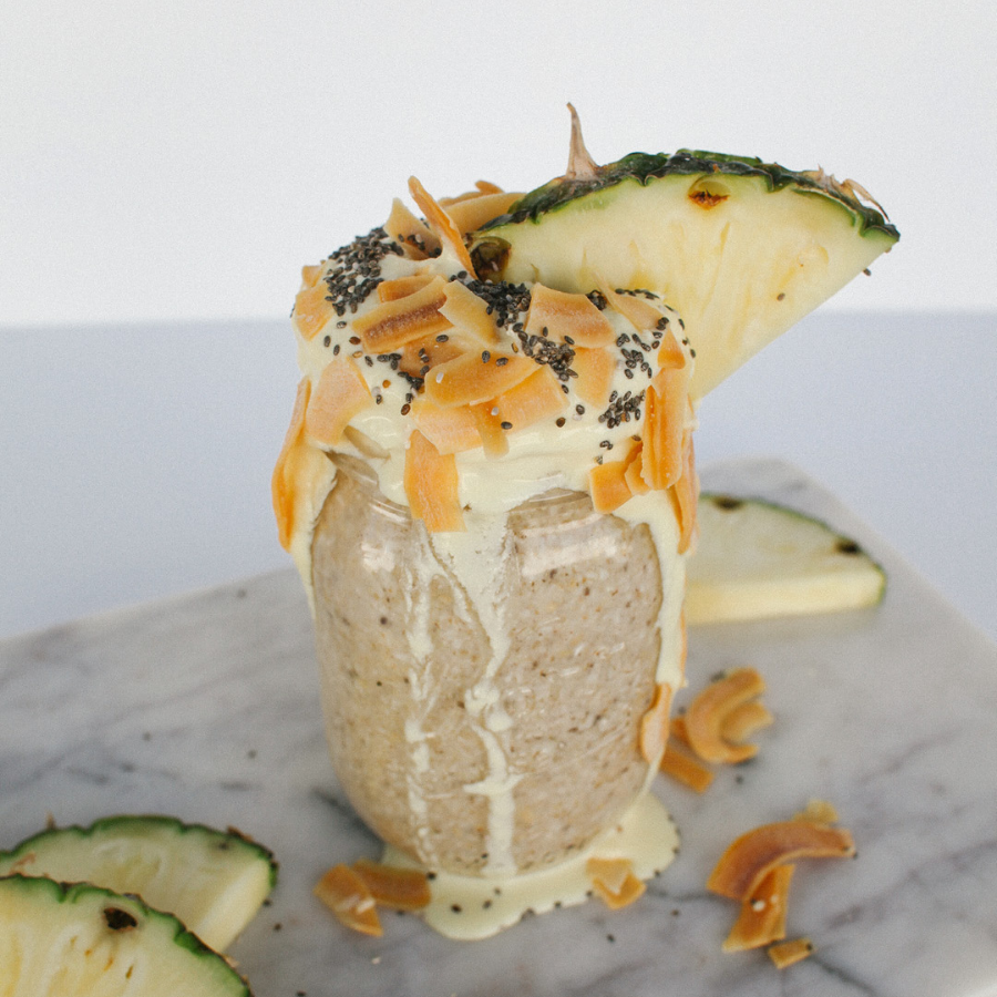 Mason jar with oatmeal, chia seeds and coconut shavings, along with pineapple wedges, overflowing onto a marble board