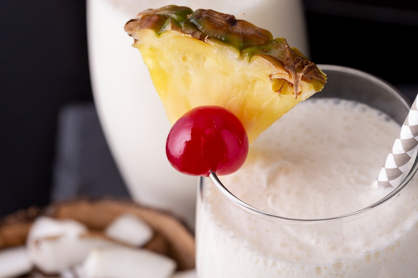 A glass of Pineapple Chia Smoothie with sliced pineapple, cherry, and a straw
