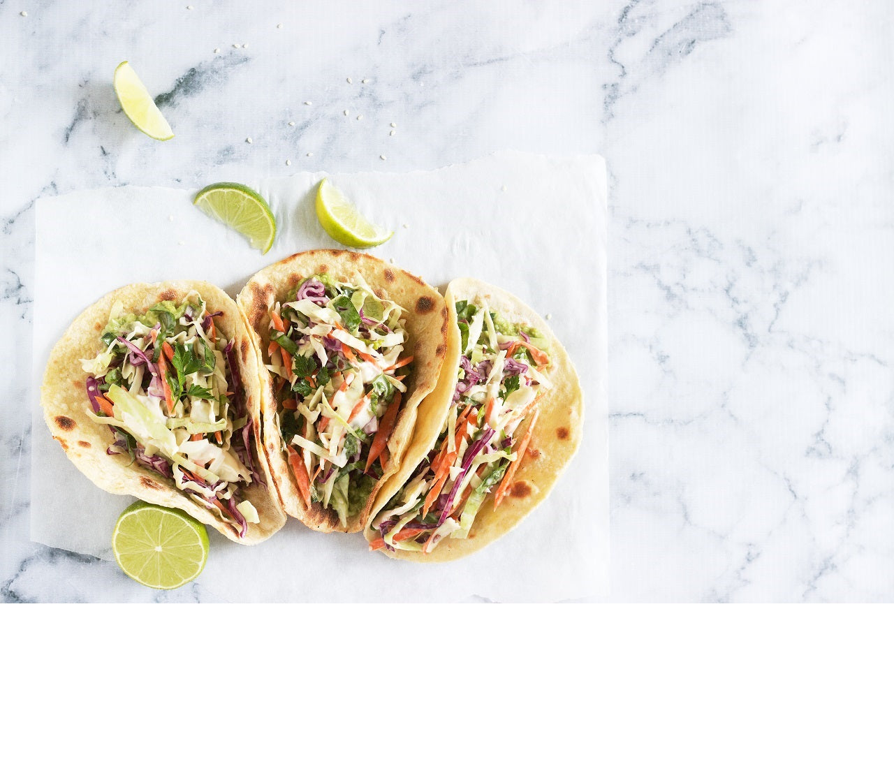 top view shot of 3 Tempeh Vegan Tacos beside 4 slices of lime on a marble surface.