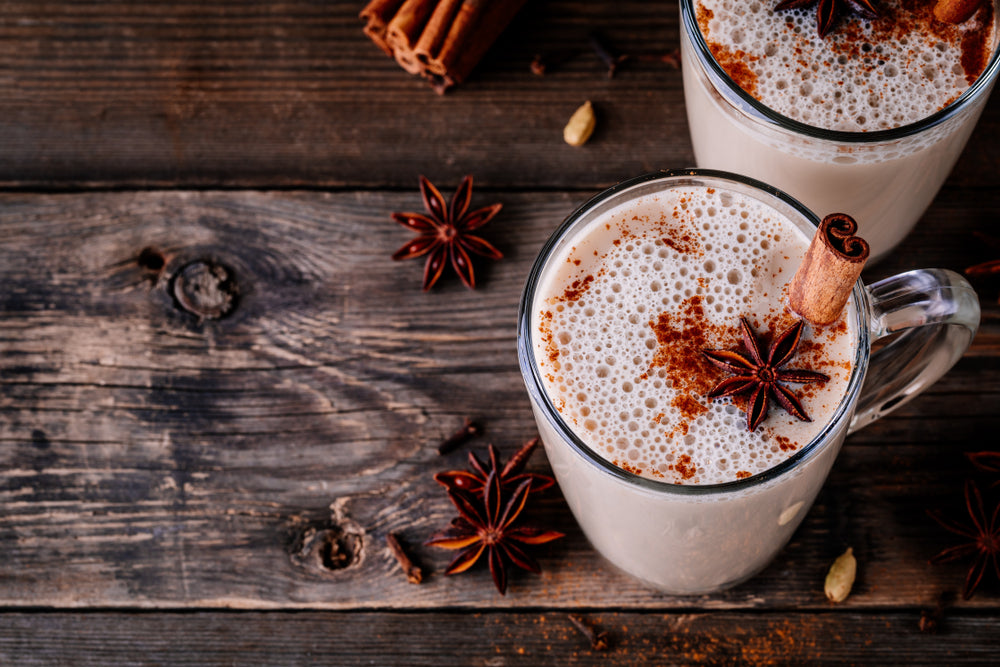 two glasses of pineapple chia cinnamon latte with cinnamon stick and star anise on top of a wooden table with star anise and a bundle of cinnamon stick on the side