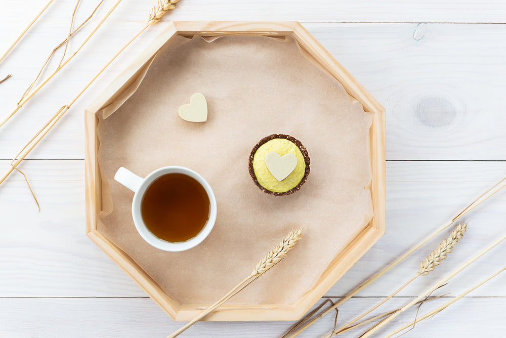 top view of a cup inside of an octagon tray with cashew and cacao pineapple chia and a yellow cupcake with a heart white shape on top surrounded by hays